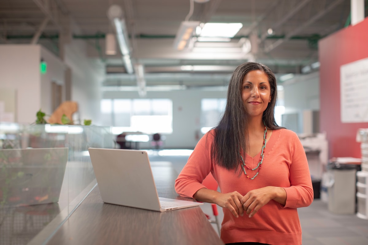 A professional standing beside an open laptop in a bright open-plan office