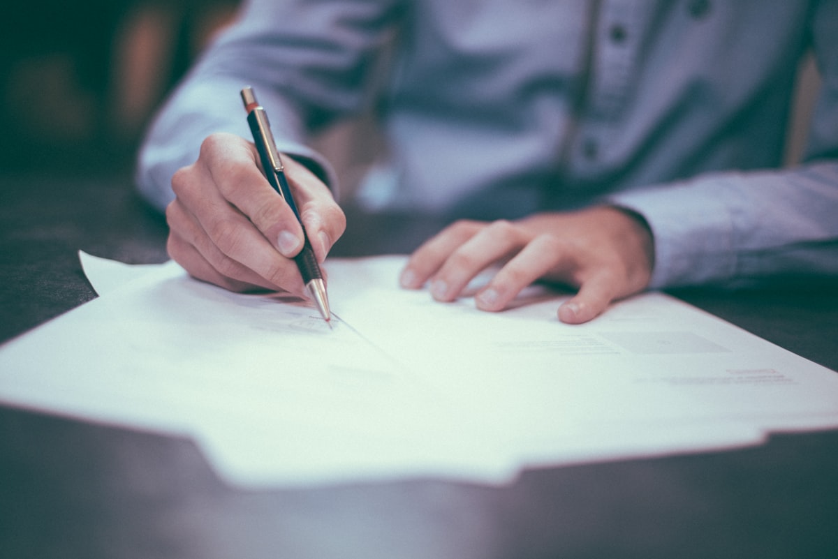 Hand signing formation paperwork with a pen at a desk